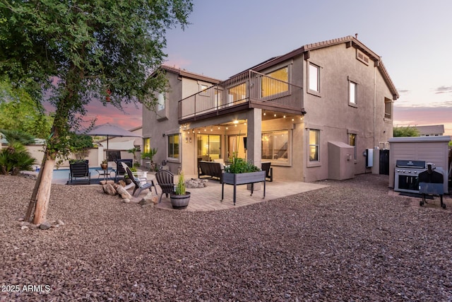 back house at dusk featuring a balcony, a hot tub, and a patio