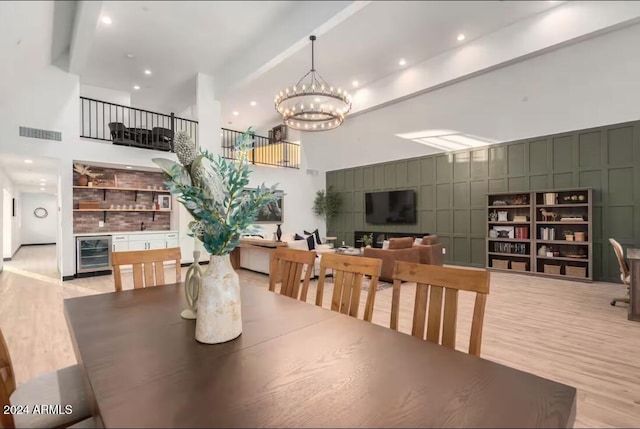 dining space with a chandelier, light hardwood / wood-style floors, a towering ceiling, and beverage cooler