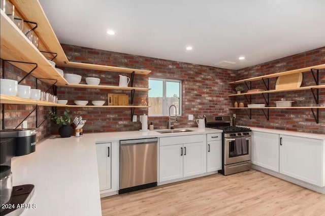 kitchen with appliances with stainless steel finishes, white cabinetry, light hardwood / wood-style floors, sink, and brick wall