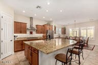 kitchen with wall chimney range hood, light stone counters, a spacious island, a kitchen bar, and light tile patterned floors