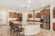 kitchen featuring a kitchen bar, a spacious island, wall chimney range hood, stainless steel refrigerator with ice dispenser, and light stone counters