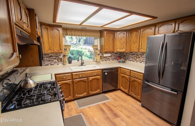 kitchen featuring black dishwasher, sink, white range with gas stovetop, stainless steel fridge, and light hardwood / wood-style floors