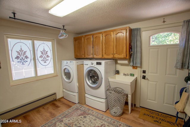 laundry room with washer and clothes dryer, a baseboard heating unit, light hardwood / wood-style flooring, cabinets, and a textured ceiling