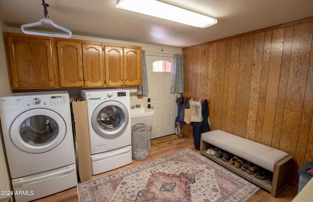 washroom featuring separate washer and dryer, a textured ceiling, wooden walls, cabinets, and light hardwood / wood-style flooring