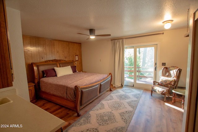 bedroom featuring hardwood / wood-style floors, ceiling fan, a textured ceiling, access to exterior, and wooden walls