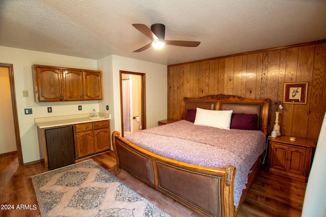 bedroom with connected bathroom, dark hardwood / wood-style floors, wooden walls, a textured ceiling, and ceiling fan