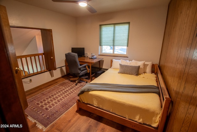 bedroom featuring hardwood / wood-style flooring, wooden walls, and ceiling fan