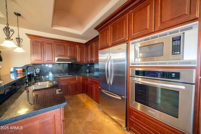 kitchen with dark stone countertops, decorative backsplash, a sink, appliances with stainless steel finishes, and decorative light fixtures