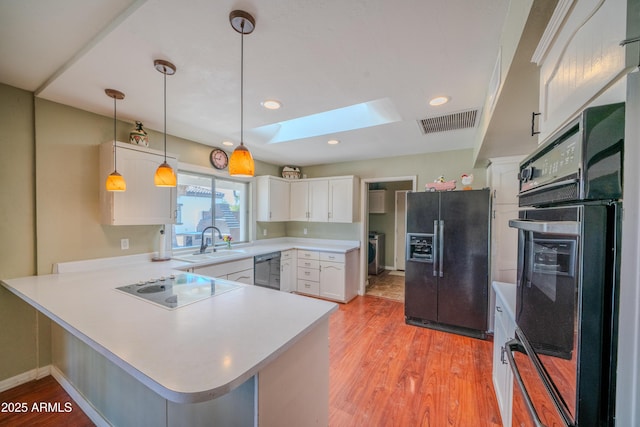 kitchen with a sink, visible vents, black appliances, a peninsula, and a skylight