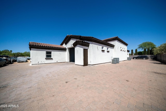 back of property with stucco siding, central air condition unit, and a tile roof