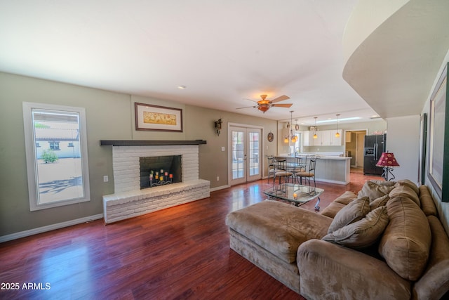 living area featuring french doors, baseboards, a fireplace, wood finished floors, and a ceiling fan