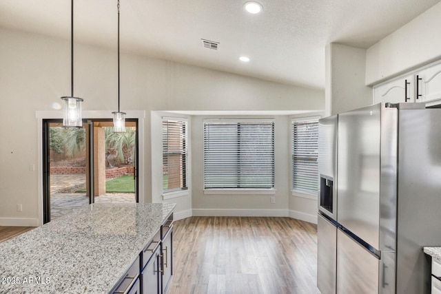 kitchen with pendant lighting, vaulted ceiling, stainless steel fridge, white cabinets, and light stone countertops