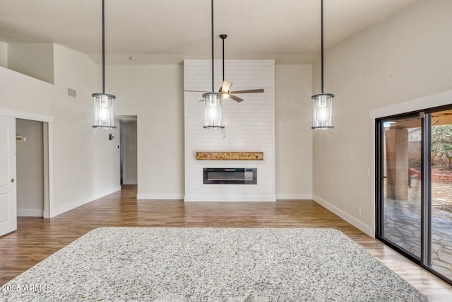 unfurnished living room with a large fireplace, ceiling fan, hardwood / wood-style floors, and a towering ceiling