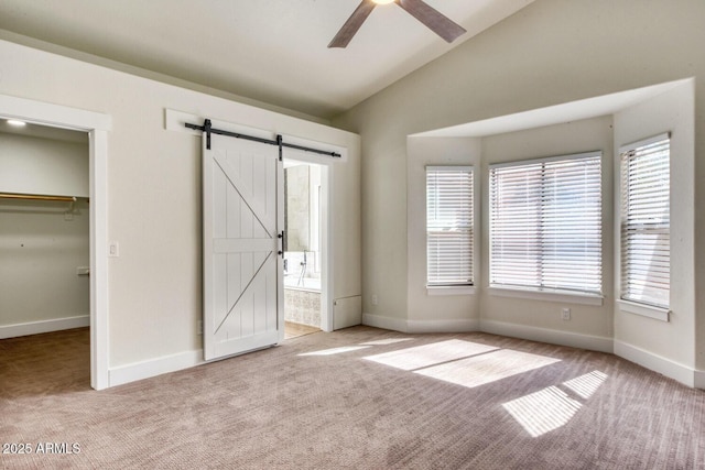 unfurnished bedroom featuring a walk in closet, lofted ceiling, ceiling fan, ensuite bathroom, and a barn door