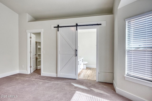 unfurnished bedroom with a walk in closet, multiple windows, a closet, ensuite bathroom, and a barn door