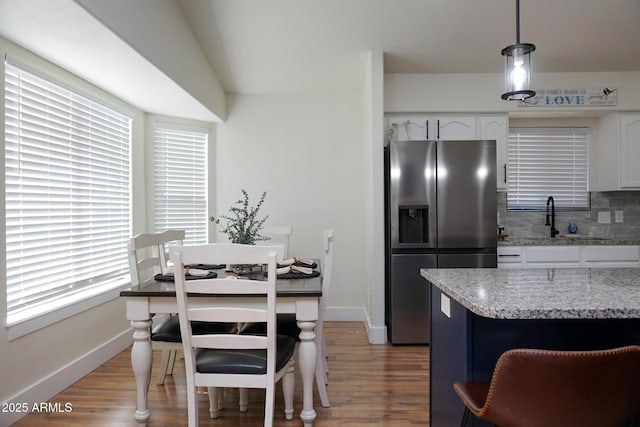 kitchen featuring light stone countertops, pendant lighting, stainless steel refrigerator with ice dispenser, white cabinetry, and backsplash