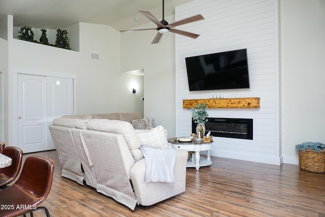 living room featuring a fireplace, wood-type flooring, high vaulted ceiling, and ceiling fan