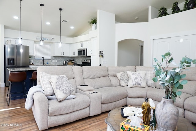 living room featuring high vaulted ceiling, sink, and light wood-type flooring