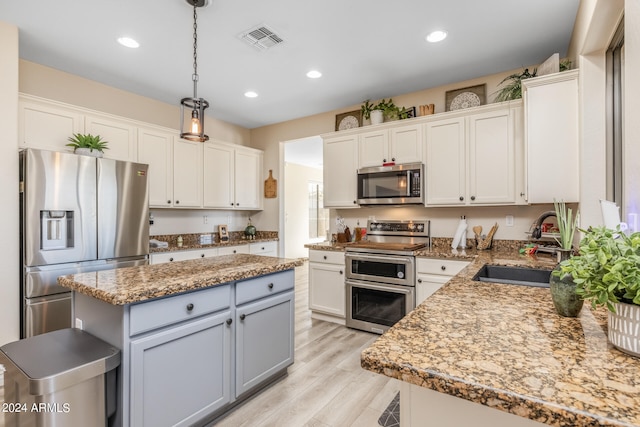 kitchen with light wood-type flooring, decorative light fixtures, sink, white cabinets, and appliances with stainless steel finishes