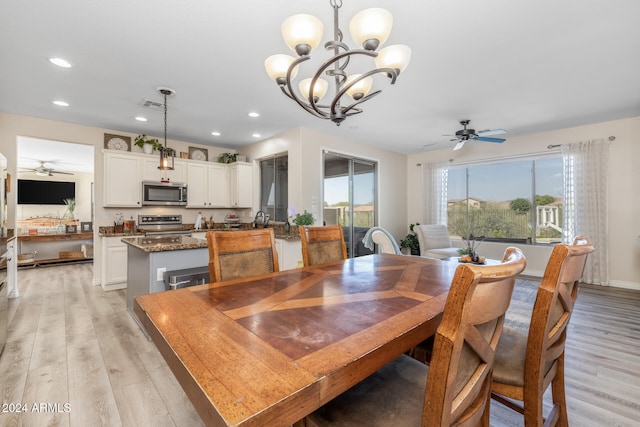 dining space with ceiling fan with notable chandelier and light hardwood / wood-style flooring