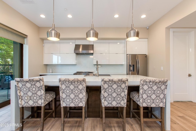 kitchen with stainless steel fridge, wall chimney exhaust hood, modern cabinets, and white cabinetry
