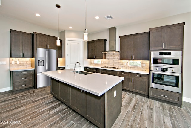 kitchen with pendant lighting, tasteful backsplash, stainless steel appliances, sink, and wall chimney exhaust hood