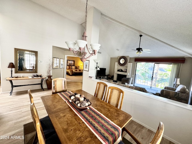 dining space with brick wall, light hardwood / wood-style floors, high vaulted ceiling, a textured ceiling, and ceiling fan with notable chandelier