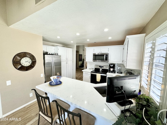 kitchen featuring white cabinetry, appliances with stainless steel finishes, light stone counters, and light hardwood / wood-style floors