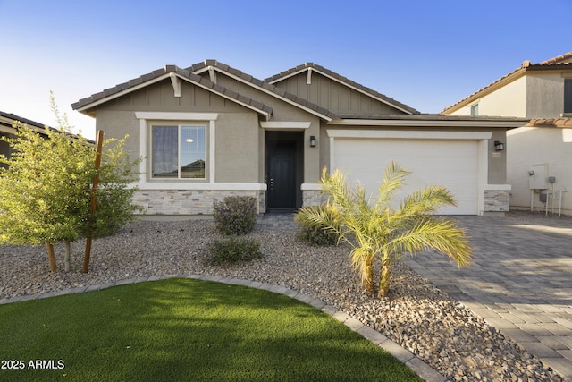 view of front of property featuring a tile roof, stone siding, an attached garage, a front yard, and decorative driveway