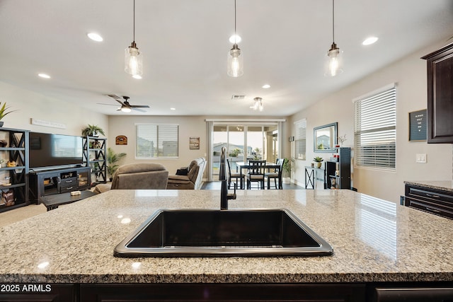 kitchen with dark brown cabinets, light stone countertops, open floor plan, and a sink
