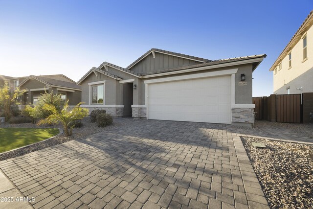 single story home with a tile roof, stone siding, fence, a garage, and decorative driveway