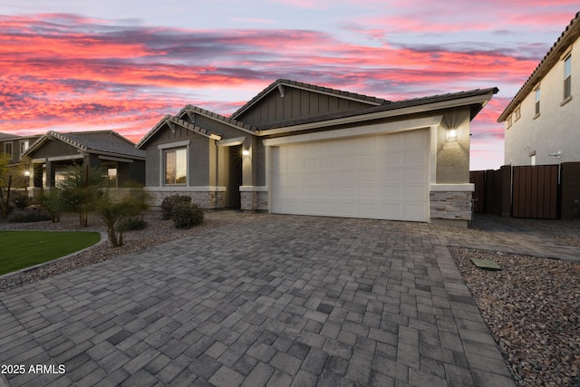 view of front of house with fence, an attached garage, a tile roof, decorative driveway, and stone siding