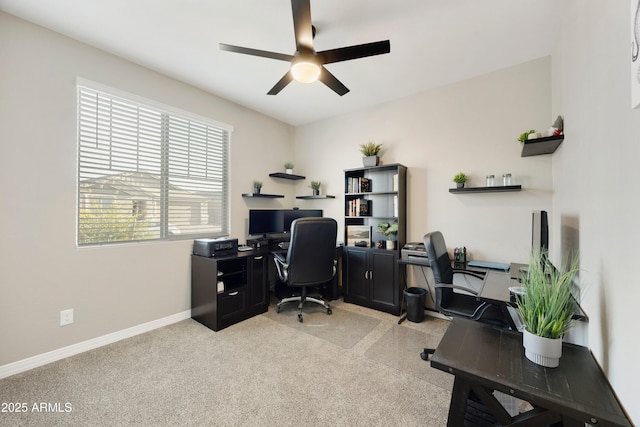 office space featuring baseboards, a ceiling fan, and light carpet