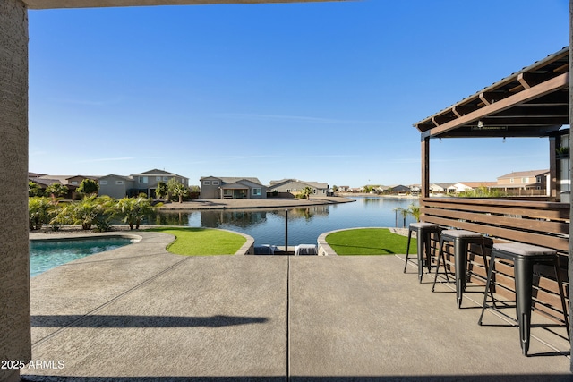 view of patio with outdoor dry bar, an outdoor pool, a water view, and a residential view