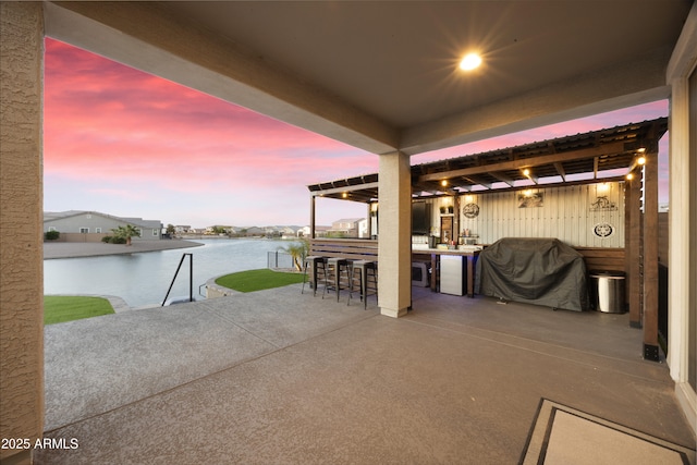 patio terrace at dusk featuring outdoor dry bar, a water view, and a grill
