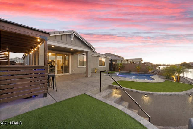 back of property at dusk featuring a yard, a fenced in pool, a patio, and a fenced backyard