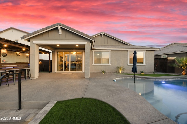back of house at dusk with a patio area, board and batten siding, outdoor dry bar, fence, and a fenced in pool