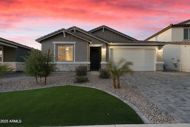 view of front of house with stone siding, an attached garage, a lawn, board and batten siding, and decorative driveway