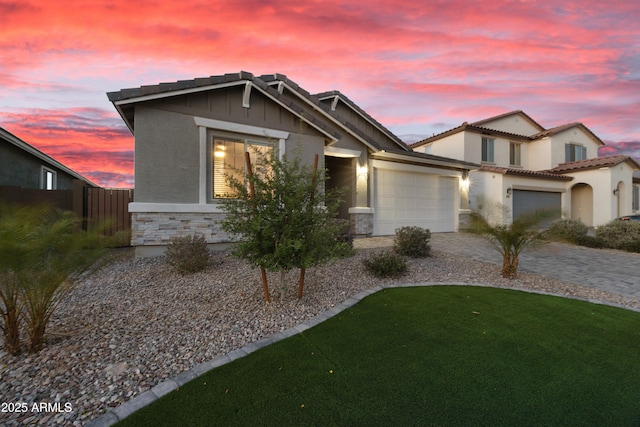 view of front of property with a tiled roof, stone siding, fence, a garage, and stucco siding