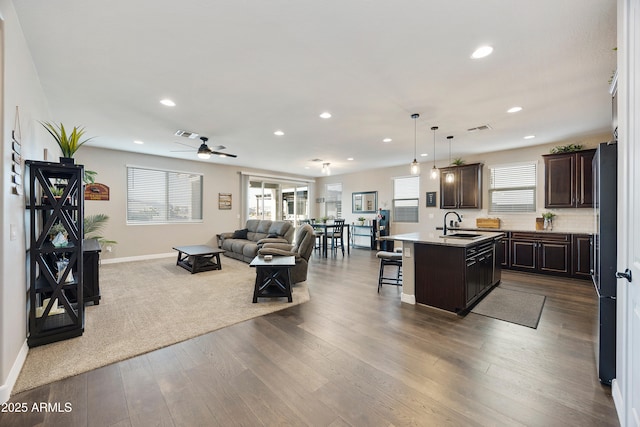 kitchen with an island with sink, a sink, dark brown cabinetry, open floor plan, and a breakfast bar area
