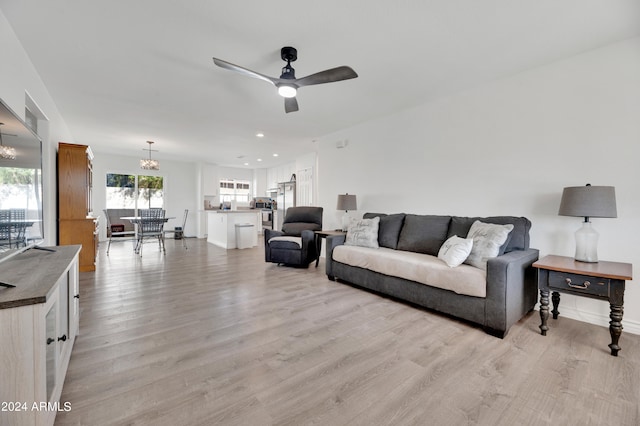 living room with ceiling fan with notable chandelier and light hardwood / wood-style floors