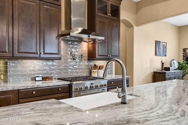 kitchen featuring tasteful backsplash, high end stainless steel range oven, dark brown cabinetry, light stone countertops, and wall chimney exhaust hood