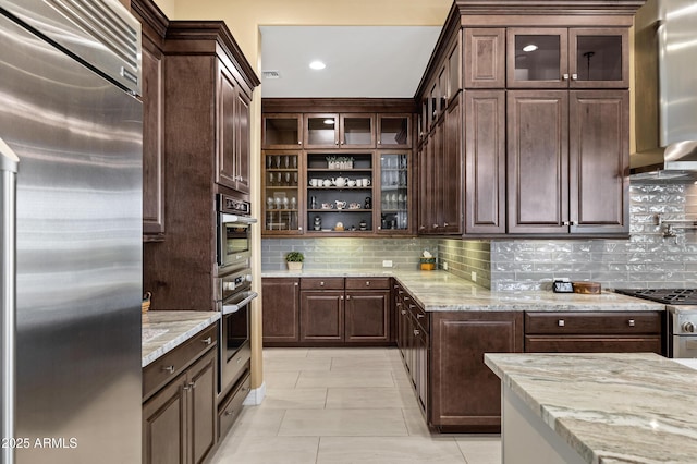 kitchen featuring appliances with stainless steel finishes, dark brown cabinets, light stone counters, and decorative backsplash