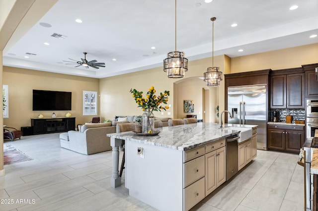 kitchen with stainless steel appliances, light stone countertops, a kitchen bar, decorative light fixtures, and a large island with sink