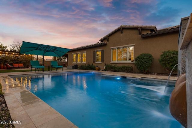 pool at dusk featuring pool water feature