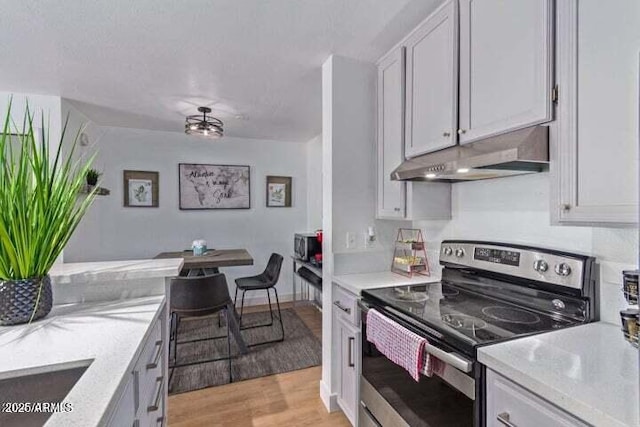 kitchen with light wood-type flooring, white cabinetry, under cabinet range hood, and stainless steel electric stove