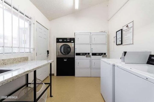 community laundry room with light floors, washer and clothes dryer, a textured ceiling, and stacked washing maching and dryer