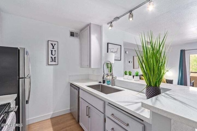 kitchen featuring light stone counters, a sink, light wood finished floors, dishwasher, and visible vents