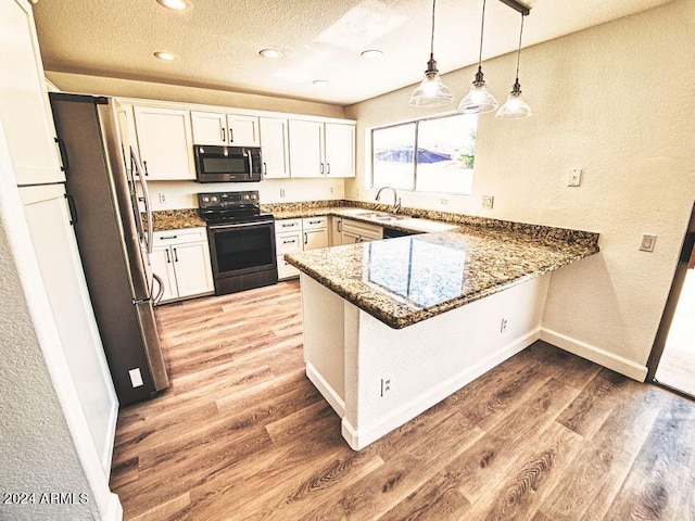 kitchen featuring kitchen peninsula, appliances with stainless steel finishes, decorative light fixtures, and light hardwood / wood-style floors