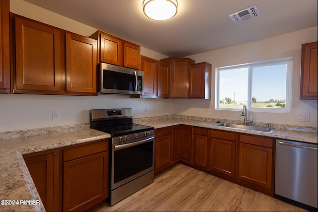 kitchen with light stone counters, stainless steel appliances, light wood-type flooring, and sink